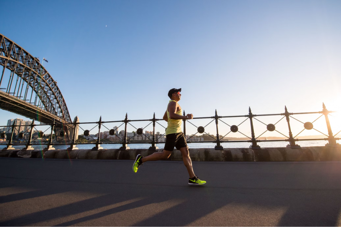 Man running by a river with a bridge behind him