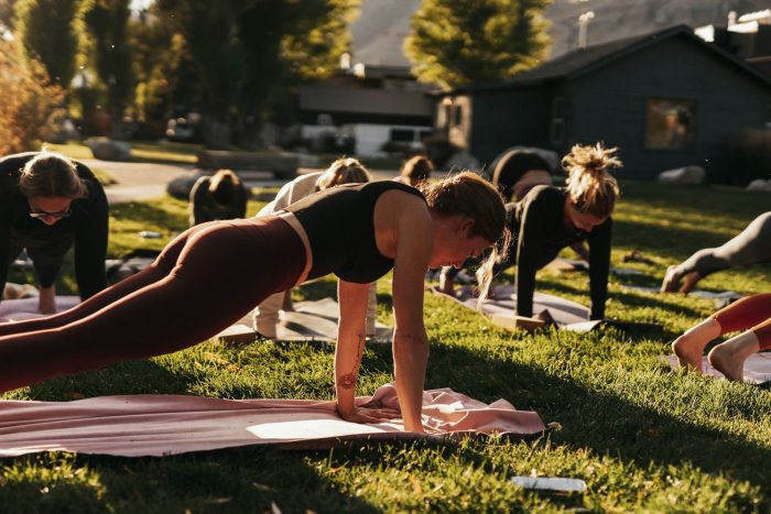 A fitness group in an outdoor space performing a plank on fitness mats