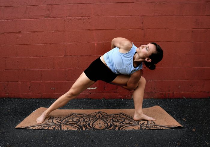 Woman stood on a mat with her legs wide apart leaning to one side with her arms around her knee stretching her hips