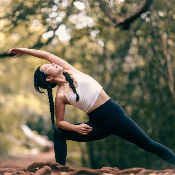 Woman stretching in a forrest with her legs in a wide stance leaning to her left