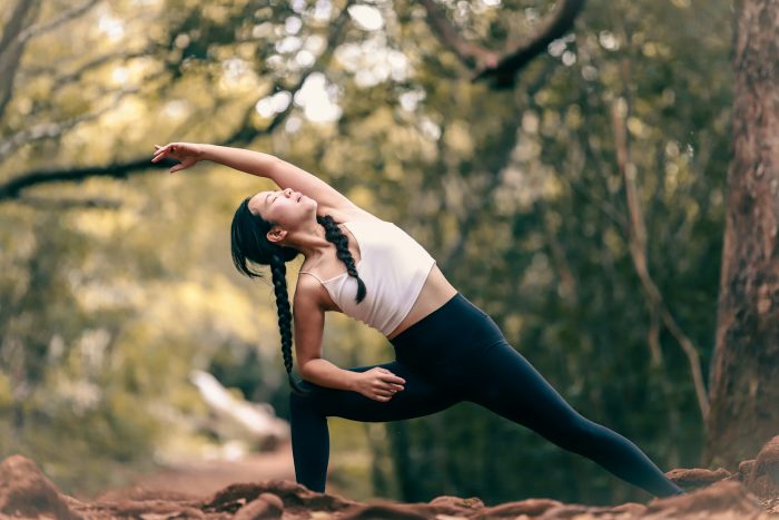 Woman stretching in a forrest with her legs in a wide stance leaning to her left