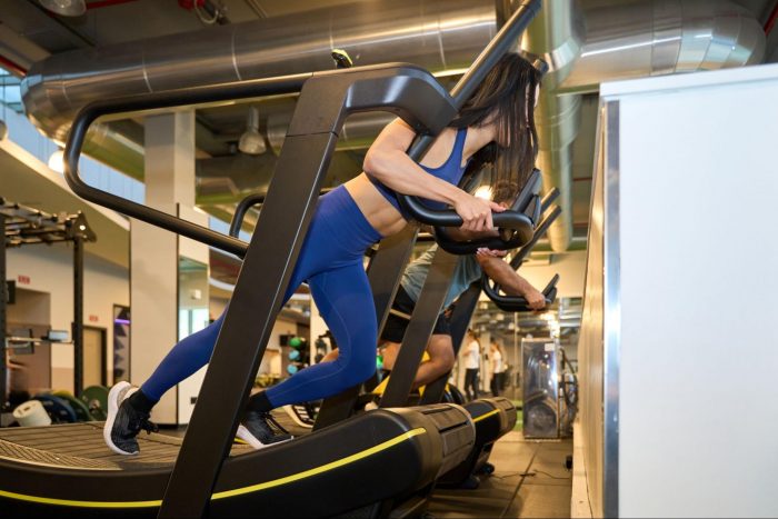 Woman in a blue gym set leaning on a curved treadmill driving forwards
