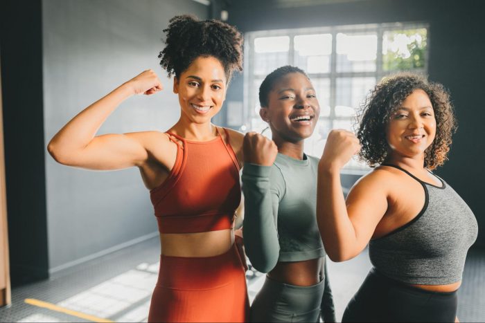 Three women flexing their muscles in a gym smiling at the camera