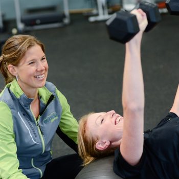 Personal trainer helping a woman perform a dumbbell bench press in a gym