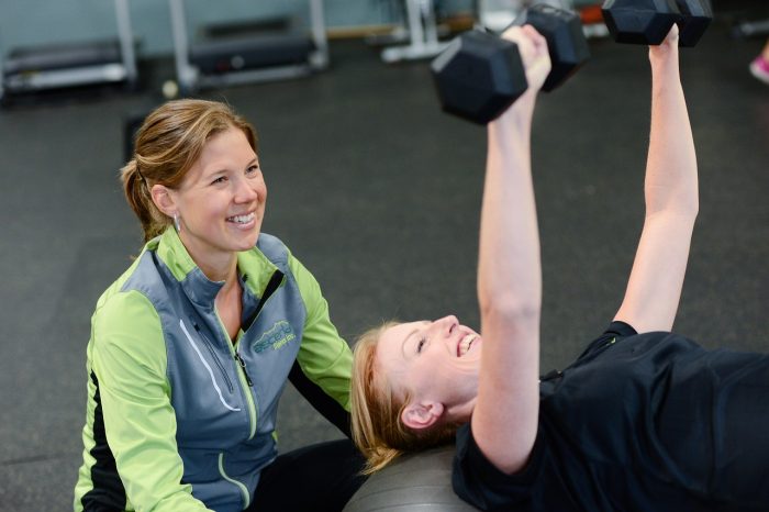 Personal trainer helping a woman perform a dumbbell bench press in a gym