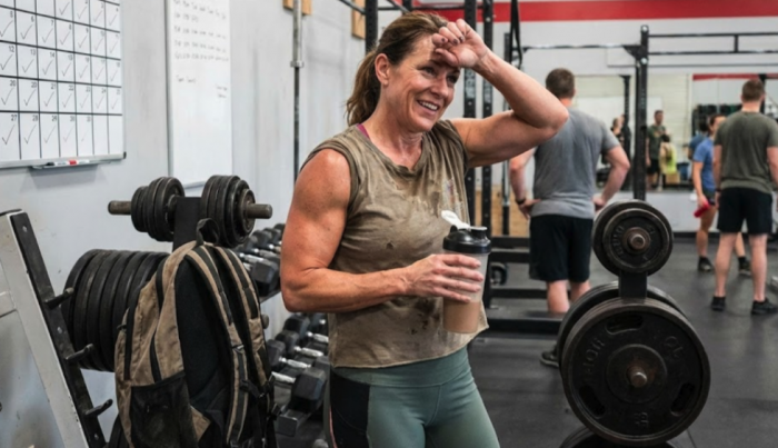Woman sweating in the gym after a workout holding a protein shake 